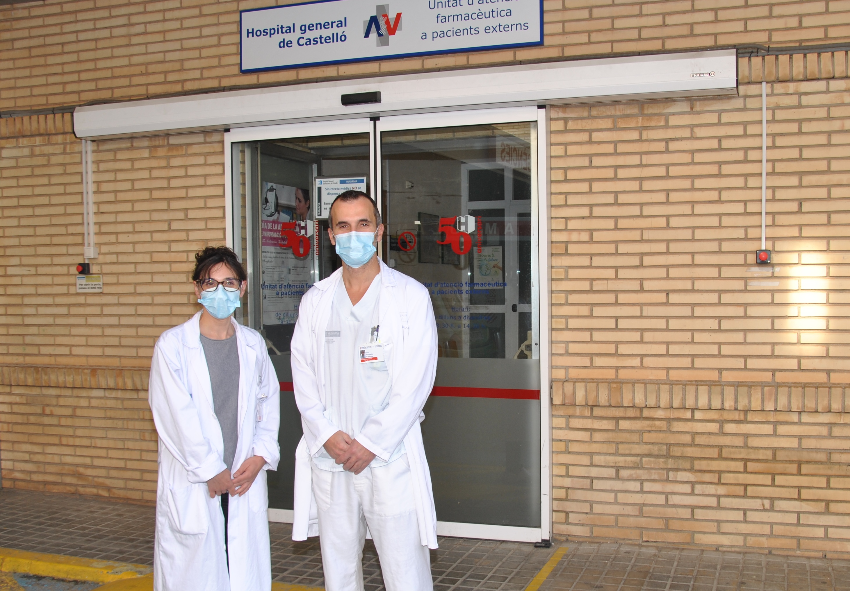 Una mujer y un hombre, especialistas en Farmacia Hospitalaria, junto a la puerta de acceso de la Unidad farmaceútica de atención a pacientes externos del Hospital General Universitario de Castellón